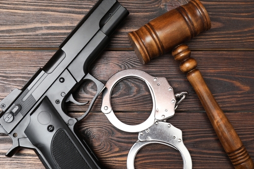 Gun - gavel - and handcuffs symbolizing gun crime charges and criminal defense cases handled by a College Station gun crimes lawyer at Cowboy Law Group.