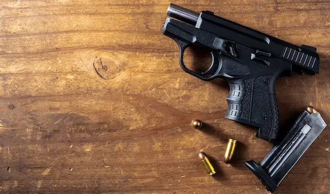 A black handgun with a magazine and bullets on a wooden table, illustrating unlawful possession of a firearm by a prohibited person.