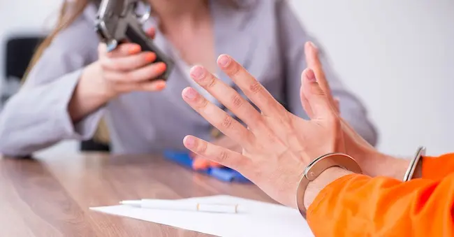 A person in handcuffs during interrogation with a firearm on the table, showing federal prosecution under federal law for weapons violations.
