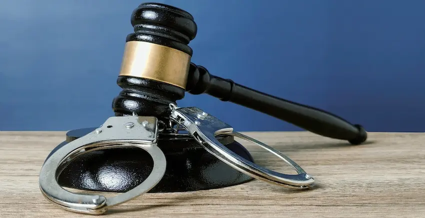 A black judge's gavel is resting on its sound block beside a pair of steel handcuffs on a wooden surface symbolizing the criminal court proceedings that determine whether a defendant will be sentenced to probation at Cowboy Law Group in Texas.