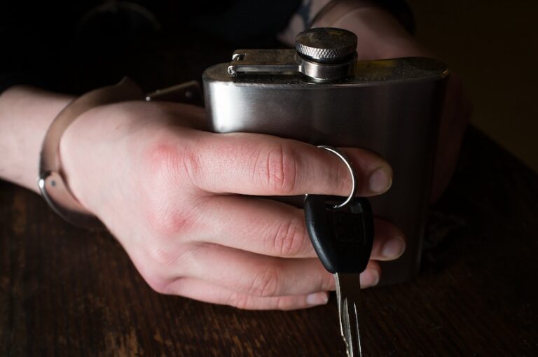 A handcuffed person is holding a flask and keys for a DWI arrest.